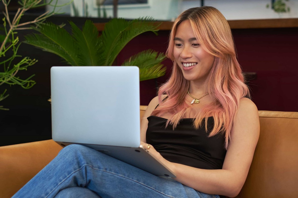 Person sitting on a couch smiling at their laptop
