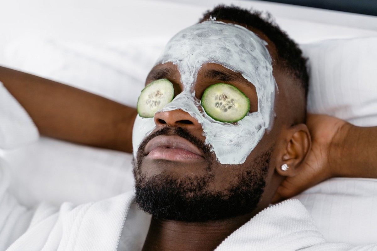 A person relaxing with sliced cucumbers on their eyes and a cream on their skin